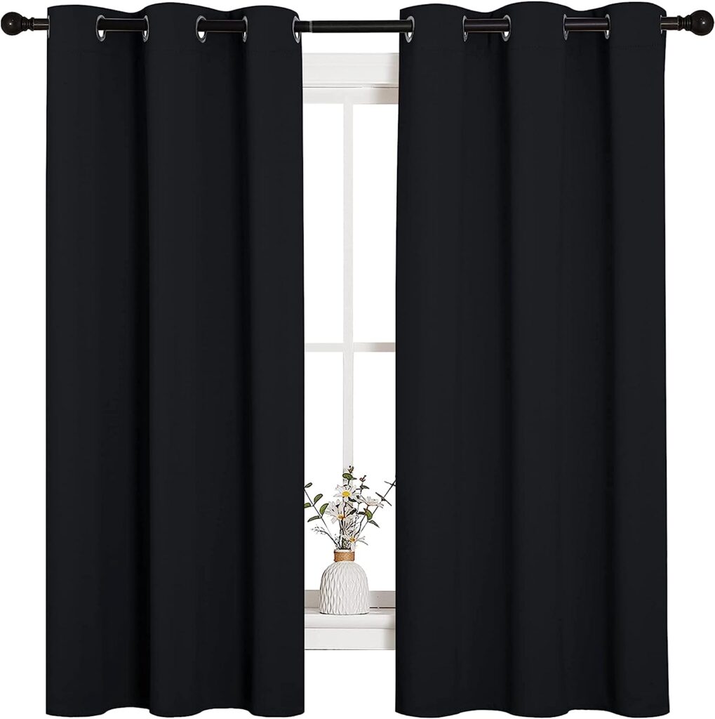 A cozy room with a window adorned by NICETOWN black thermal insulated blackout curtains hung on a black curtain rod. The curtains are drawn, blocking light effectively. A small vase with flowers sits on the windowsill, adding a touch of decor to the room.