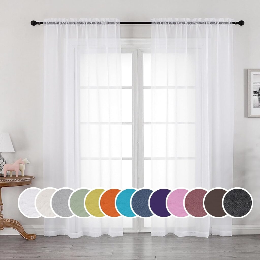 White sheer curtains hanging on a black curtain rod over a large window, allowing natural light to filter through. Below the curtains, there are swatches displaying various available colors, including white, grey, green, yellow, orange, blue, purple, pink, brown, and black. The setting includes a side table with a lamp and decorative items, creating a cozy and inviting atmosphere.