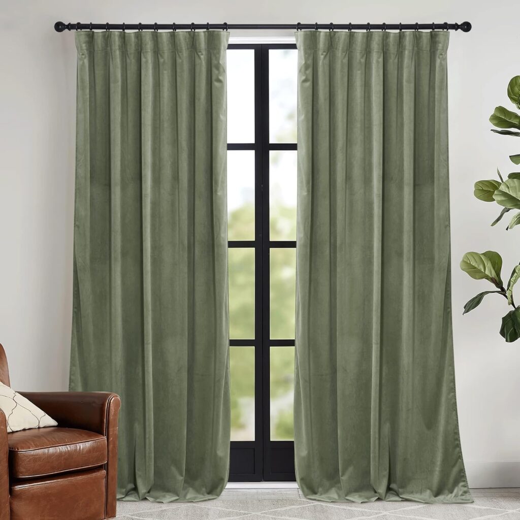 Green velvet curtains by RYB HOME, elegantly hung on a black rod, framing a tall window with a view of greenery outside. The luxurious curtains add a touch of sophistication to the room, complementing a brown leather armchair and a leafy green plant.