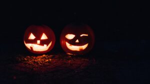 Two spooky carved and candle lit pumpkins in a dark setting.