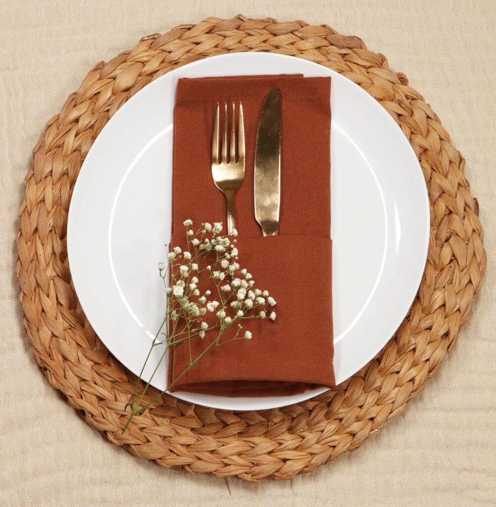 Cute setup plate with an orange napkin folded above the plate with fork, knife and a dry flower