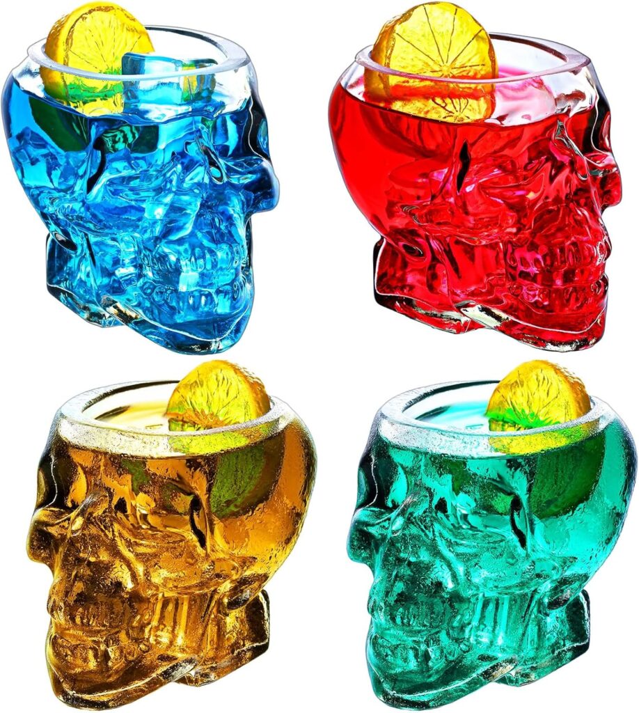 Four skull glasses all with different color liquids inside, topped with a lemon slice